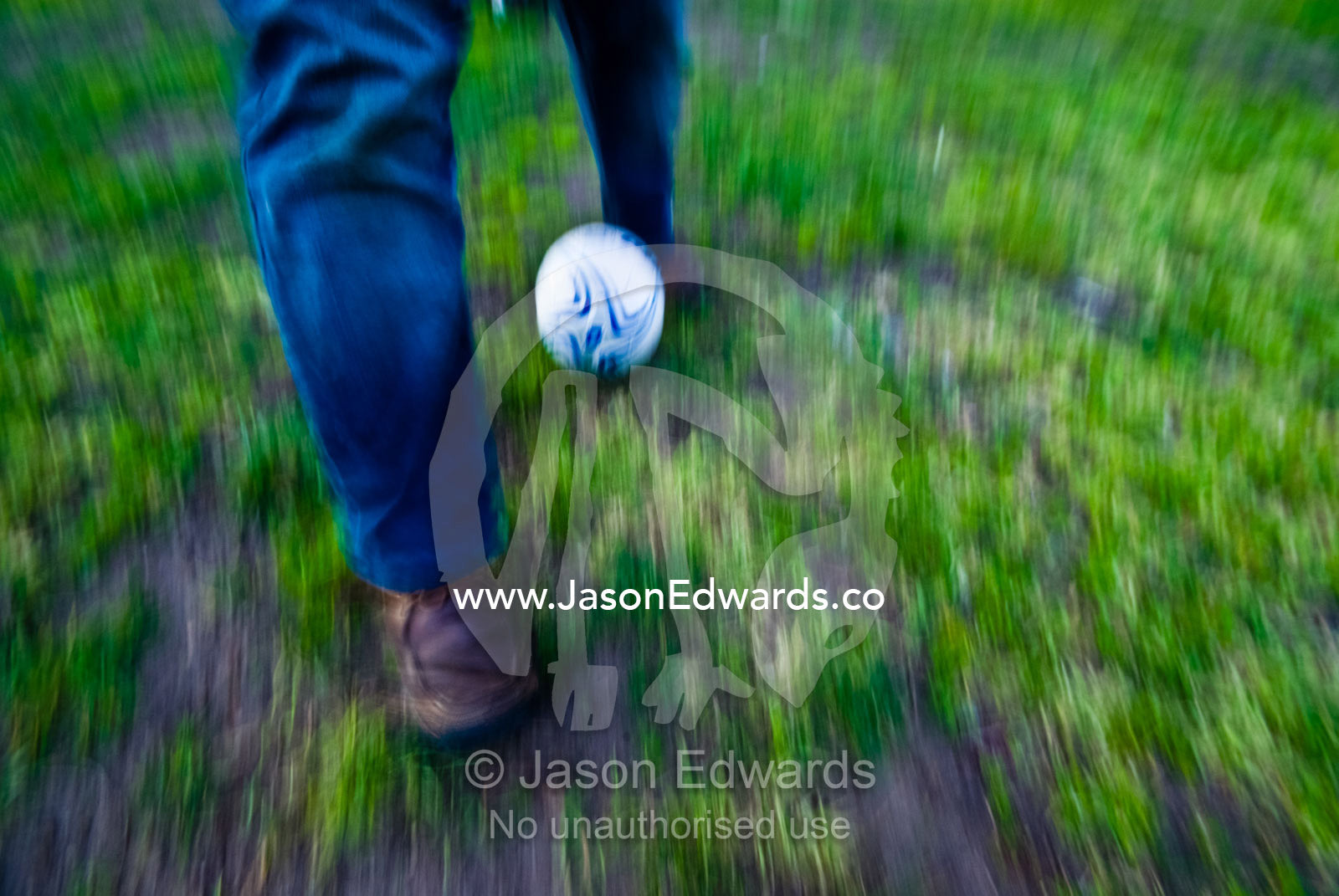 A mans legs blur as he runs through a park kicking a football. Princes Park, North Carlton, Victoria, Australia