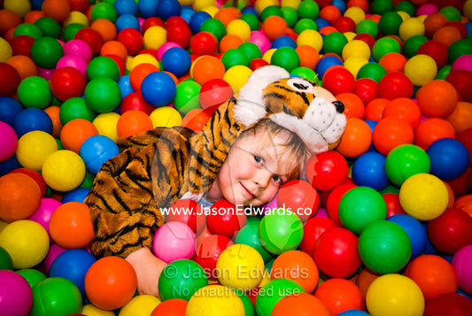A small boy dressed as a tiger playing in a pool of colorful balls. Hawthorn, Victoria, Australia