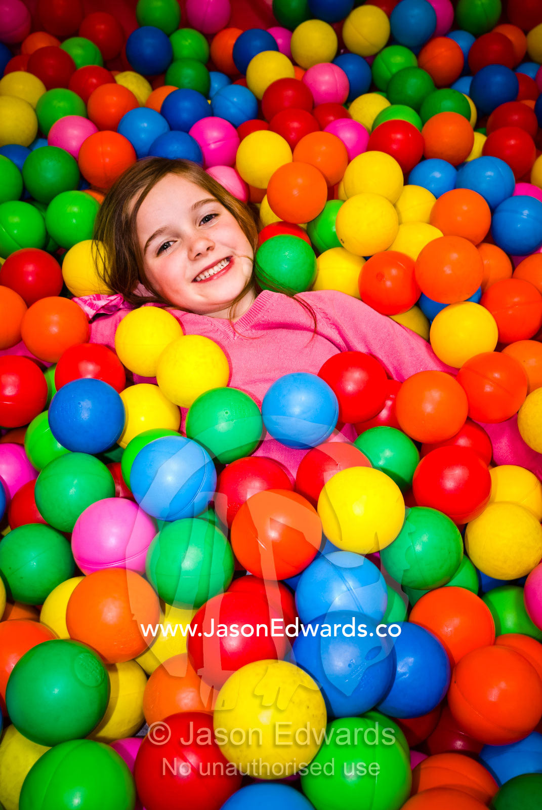 A small girl playing in a pool of colorful balls at a play center. Hawthorn, Victoria, Australia