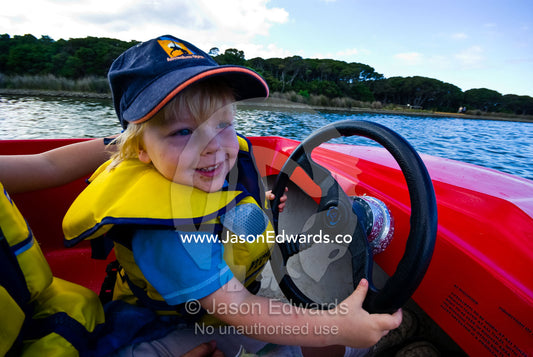 A small boy steers a children's speed boat on a lake at a carnival. Anglesea, Surf Coast, Victoria, Australia