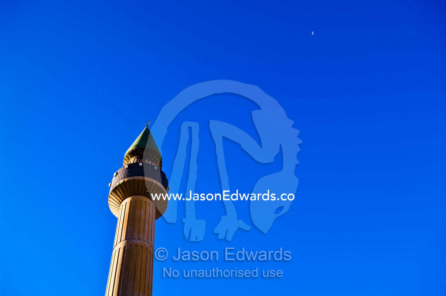 A minaret on an Islamic mosque rises into a blue sky towards the moon. Carlton North, Victoria, Australia