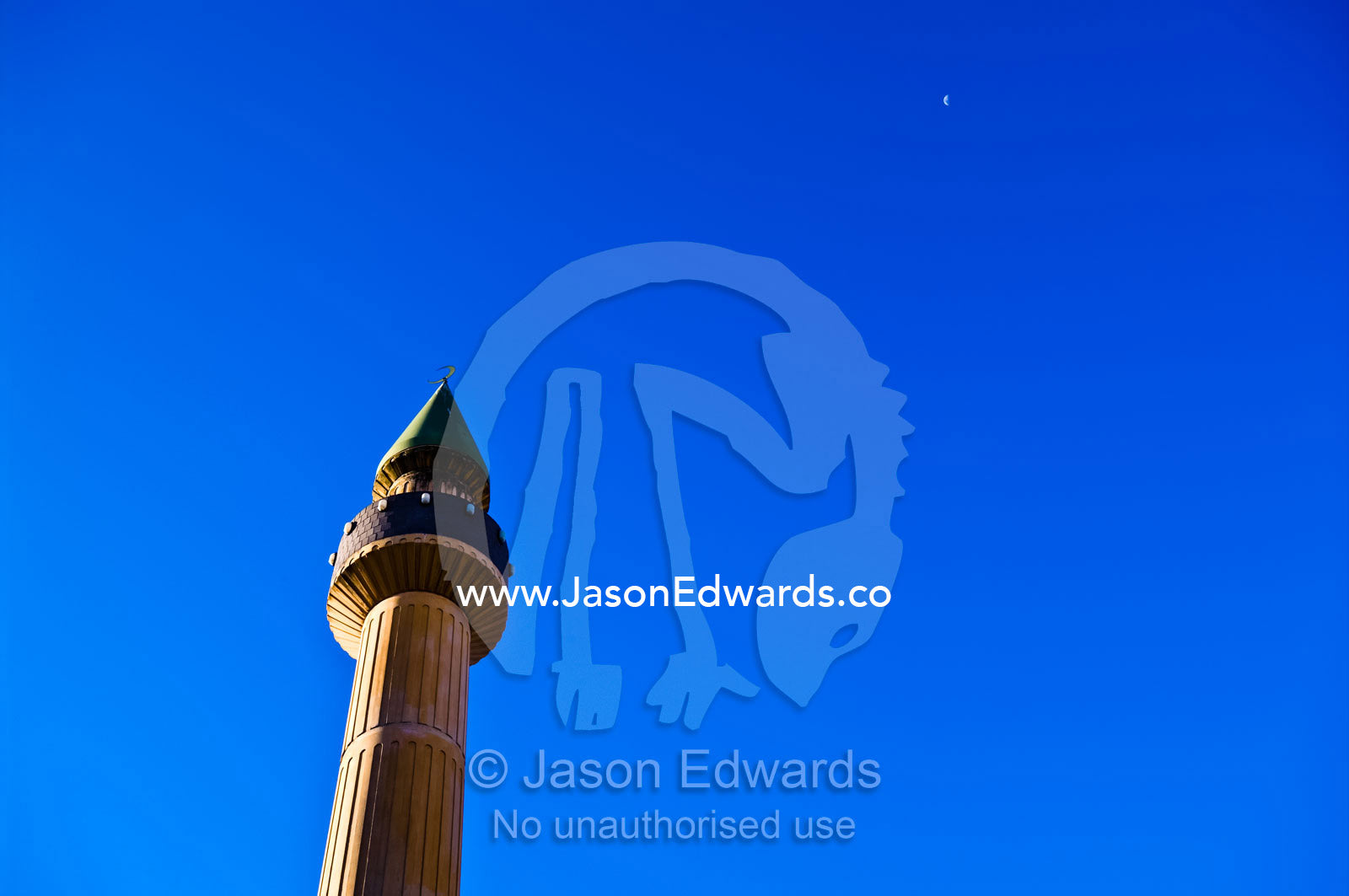 A minaret on an Islamic mosque rises into a blue sky towards the moon. Carlton North, Victoria, Australia