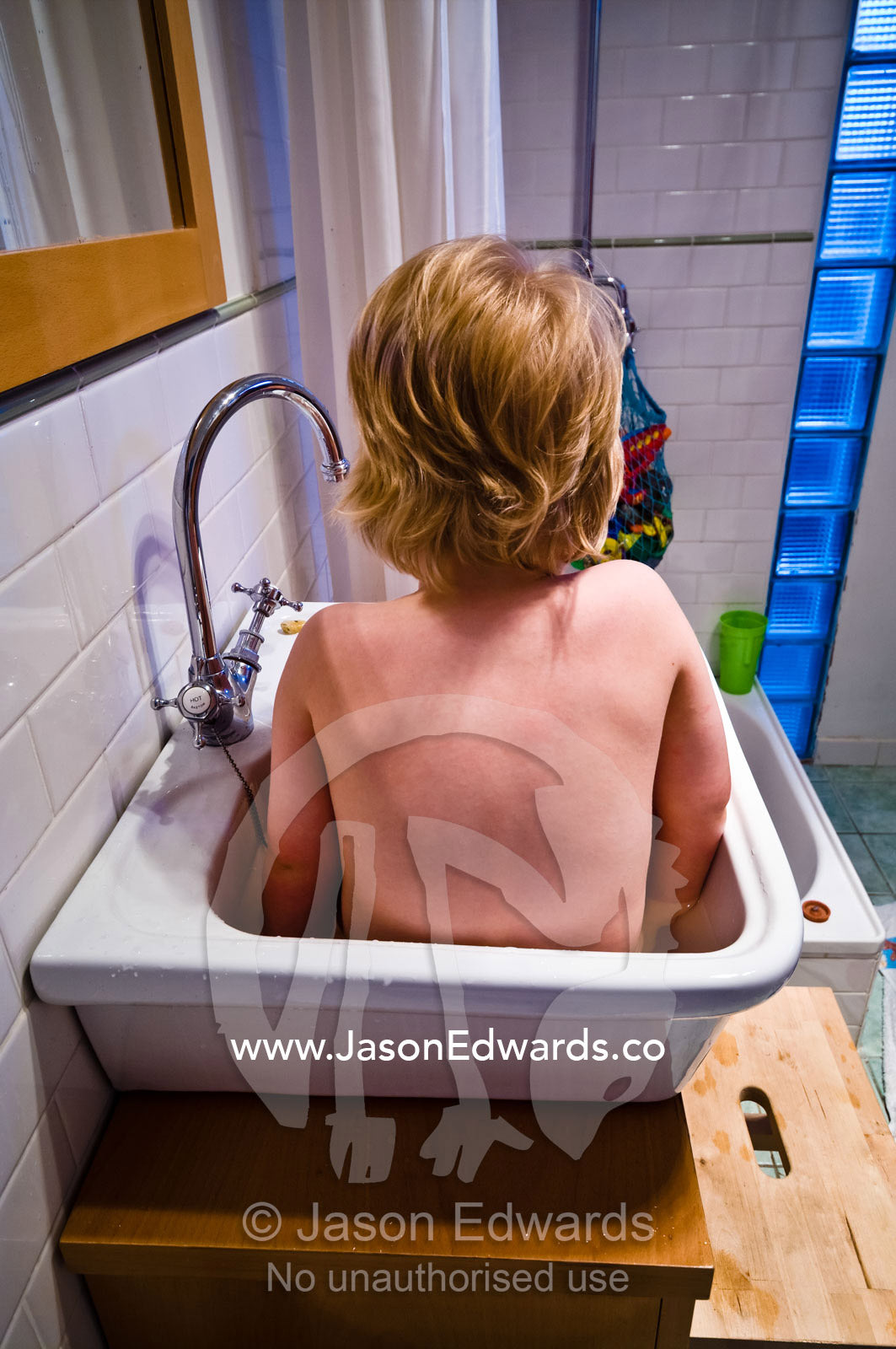 A young fair-skinned boy takes a bath in a small porcelain sink. Carlton North, Victoria, Australia