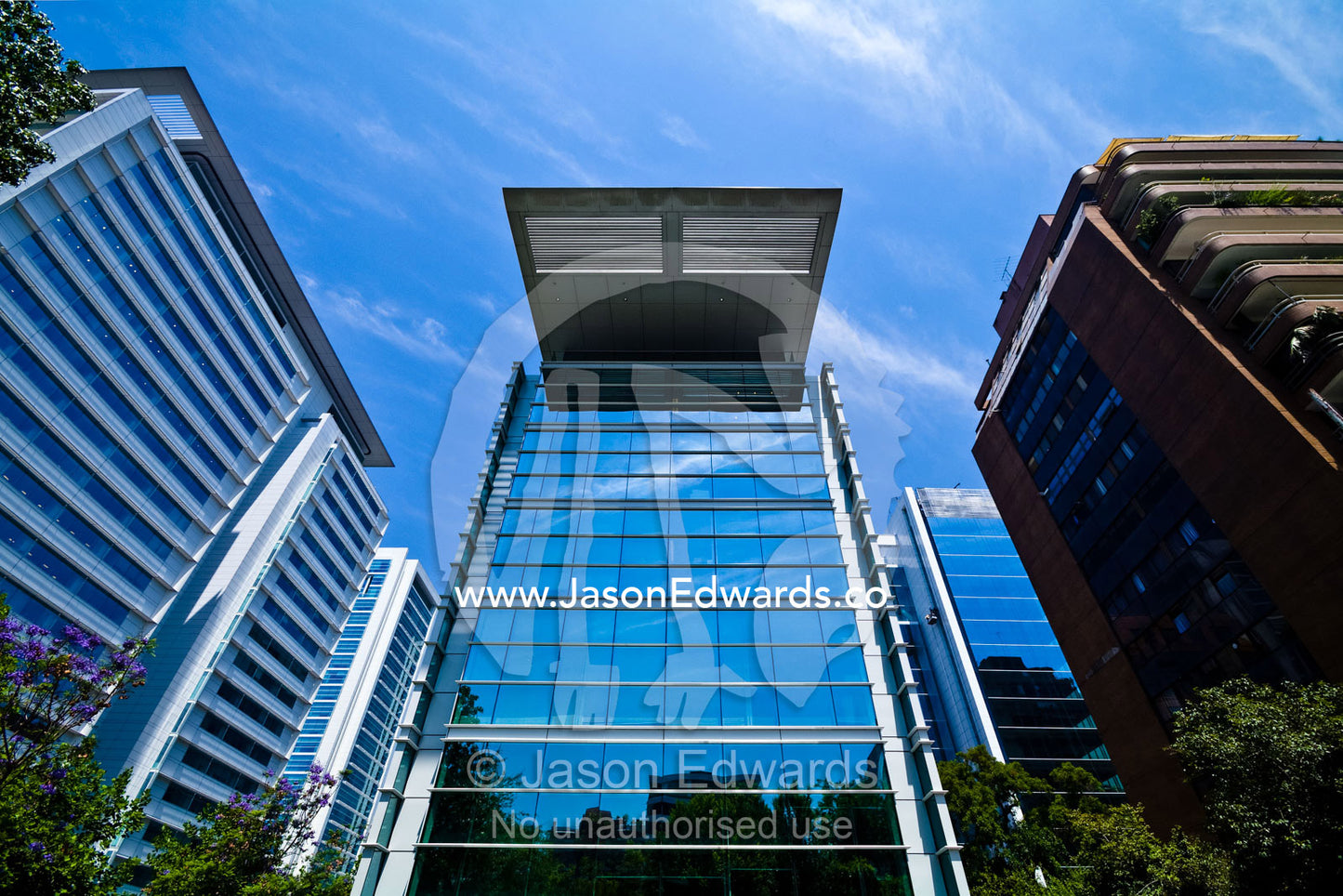 A modern glass office tower rises above trees reflecting the blue sky. Providencia, Santiago, Chile