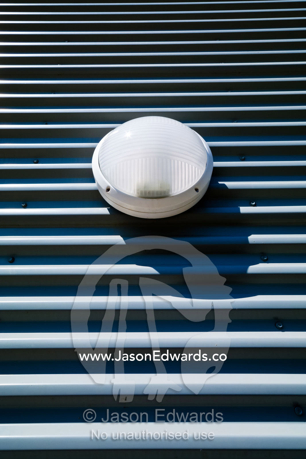 A circular plastic light bolted onto a corrugated grey steel wall. Darwin Convention Centre, Darwin, Northern Territory, Australia