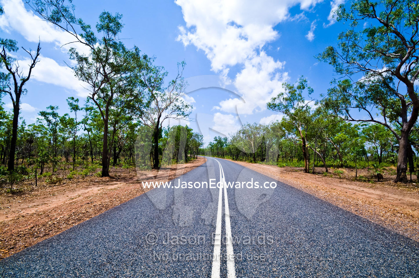 White lines run down the middle of a well-kept road in open woodland. Kakadu Highway, Northern Territory, Australia