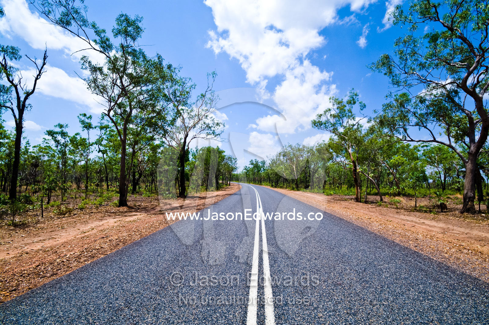 White lines run down the middle of a well-kept road in open woodland. Kakadu Highway, Northern Territory, Australia