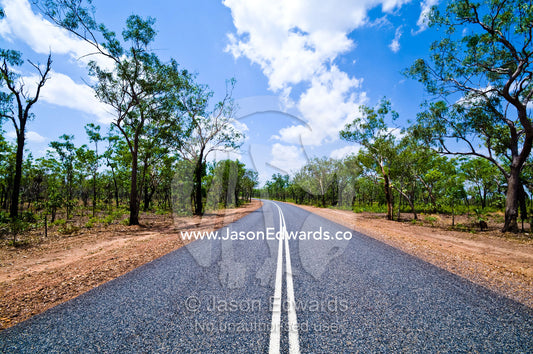 White lines run down the middle of a well-kept road in open woodland. Kakadu Highway, Northern Territory, Australia