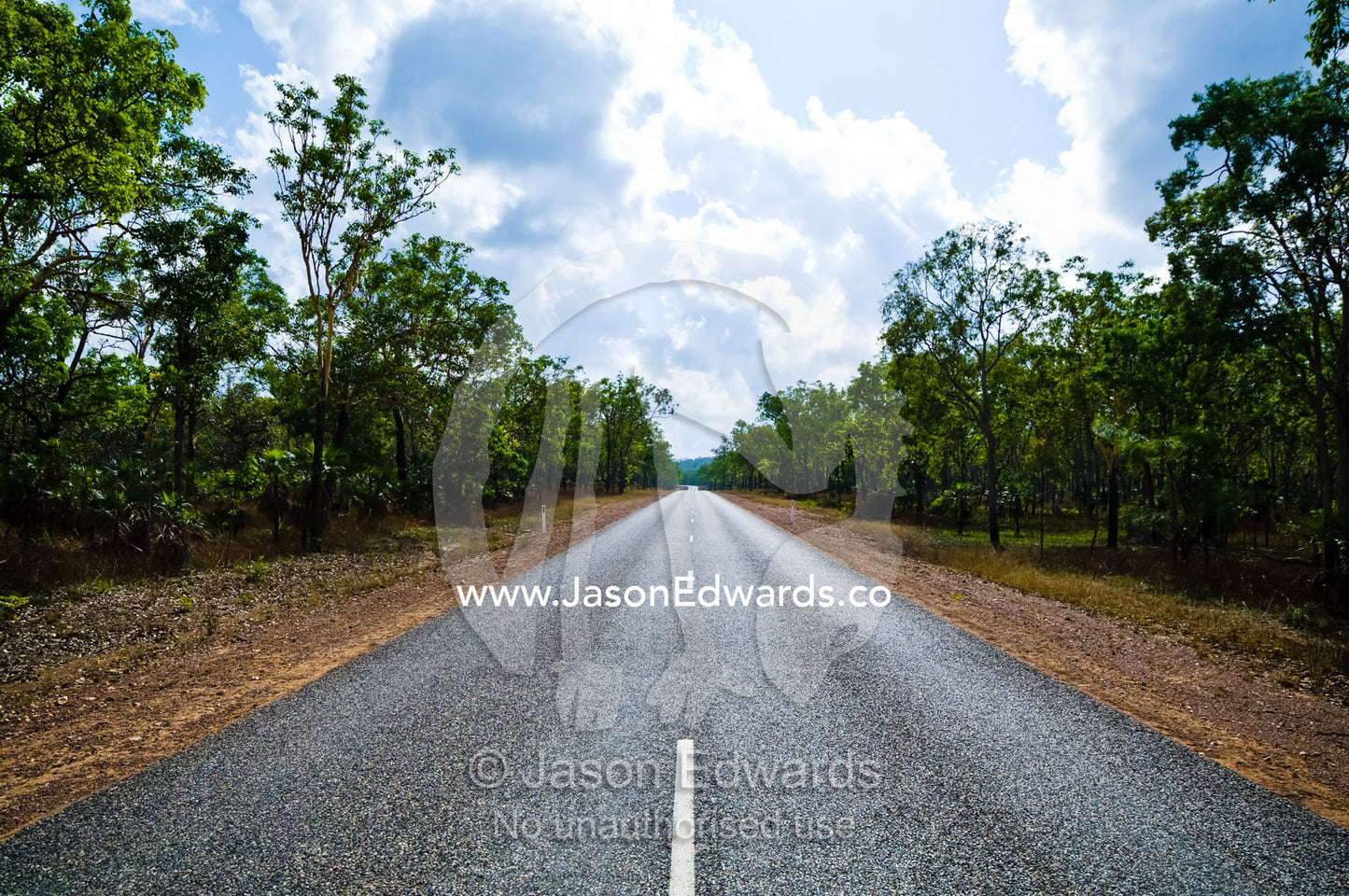 White lines run down the middle of a straight road in open woodland. Kakadu Highway, Northern Territory, Australia