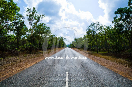 White lines run down the middle of a straight road in open woodland. Kakadu Highway, Northern Territory, Australia