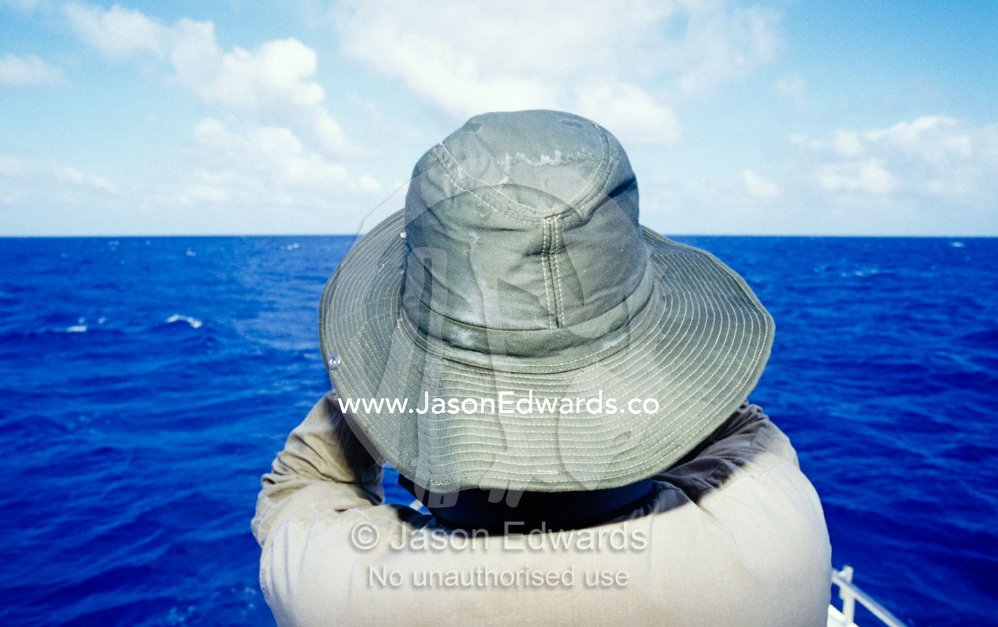 An ornithologist in a hat scans the vast ocean horizon for seabirds. Coral Sea, Queensland, Australia