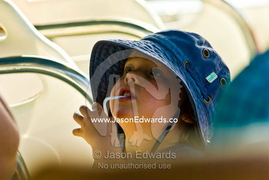 A small boy in a summer hat drinking fruit juice through a straw. Litchfield National Park, Northern Territory, Australia.