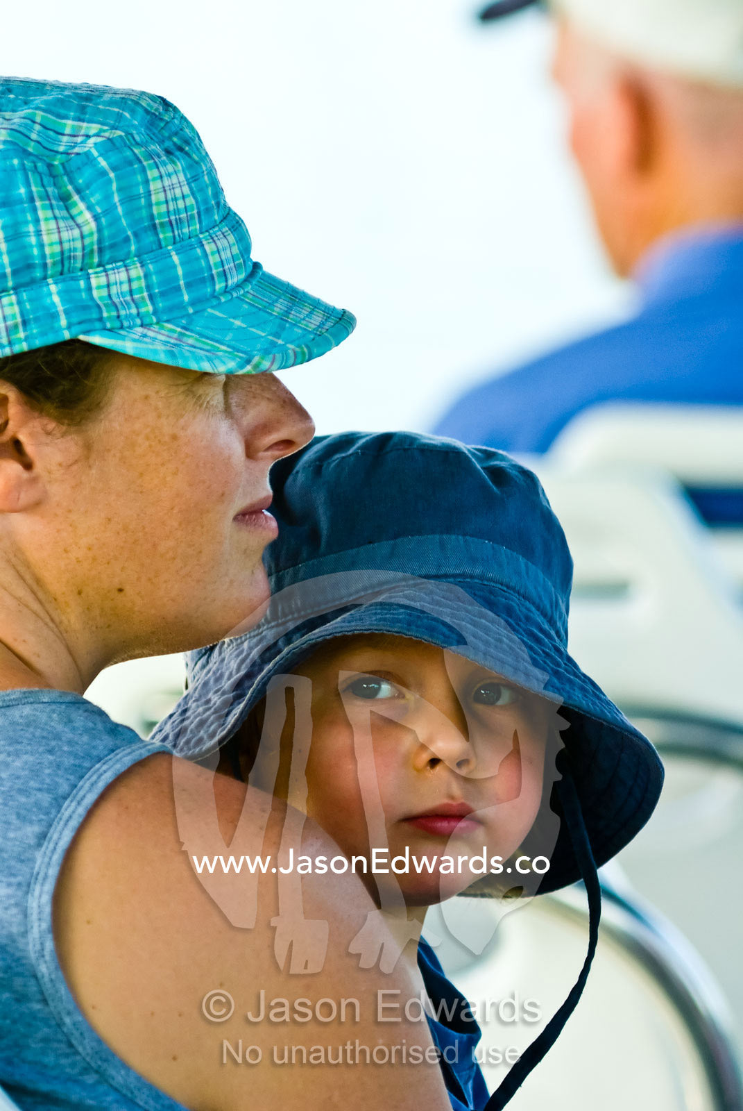 A small boy in a summer hat sits on his mother's lap on a boat cruise. Litchfield National Park, Northern Territory, Australia.