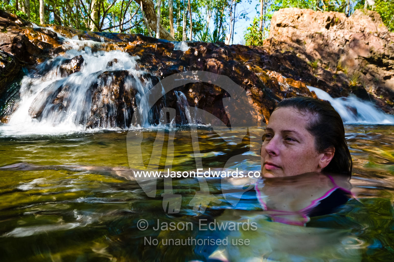A woman swimming at the base of a tropical waterfall to stay cool. Buley Rockhole, Litchfield National Park, Northern Territory, Australia.