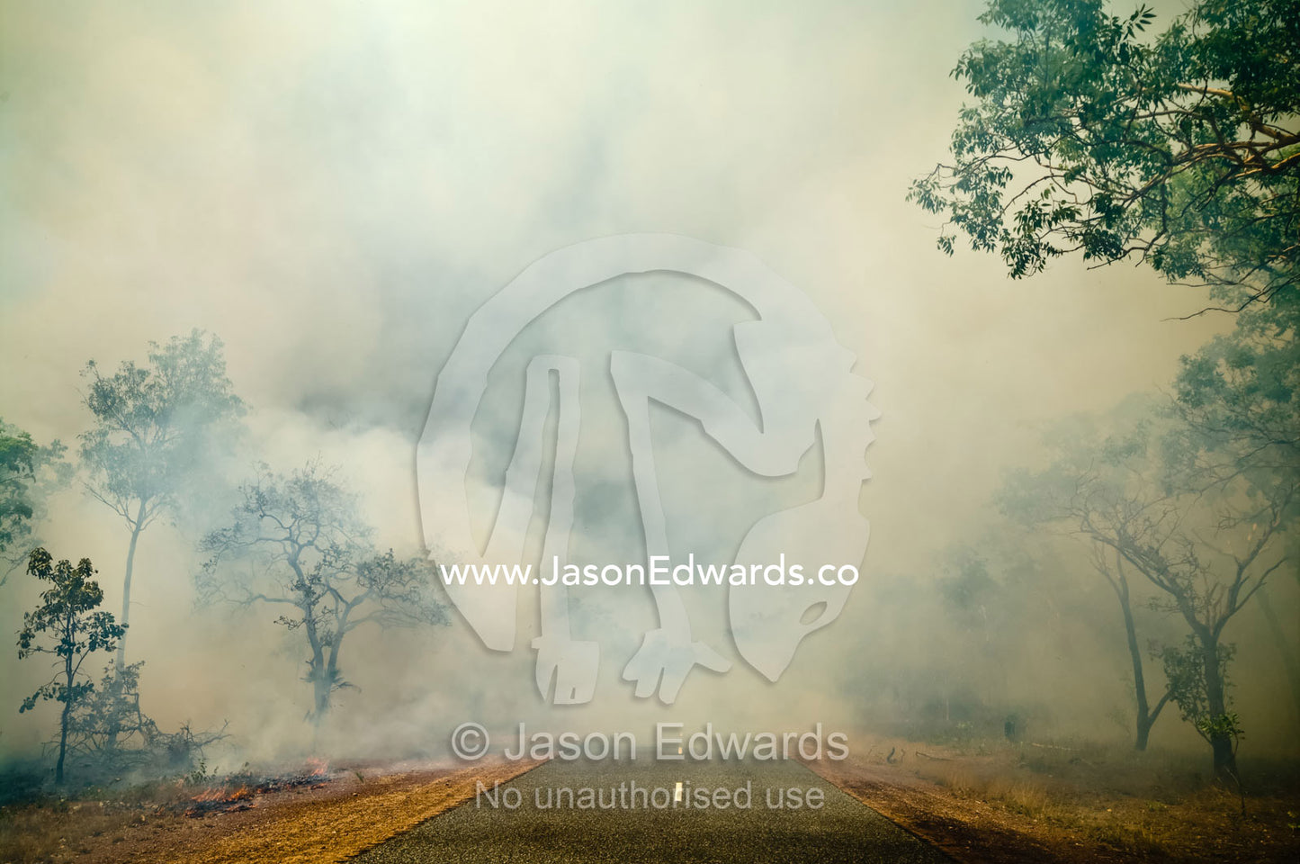 Billowing and choking smoke engulfs a country road reducing visibility. Litchfield National Park, Northern Territory, Australia.