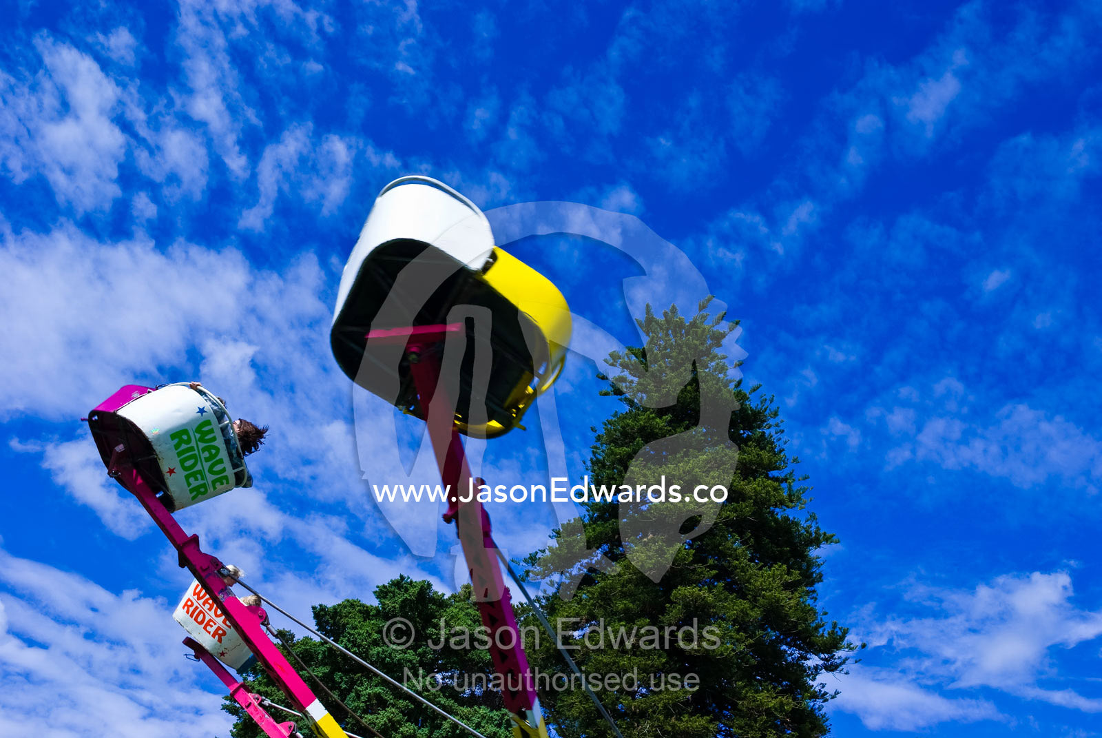 Children ride a colourful carnival ride twirling in a blue summer sky. Malvern East, Victoria, Australia.