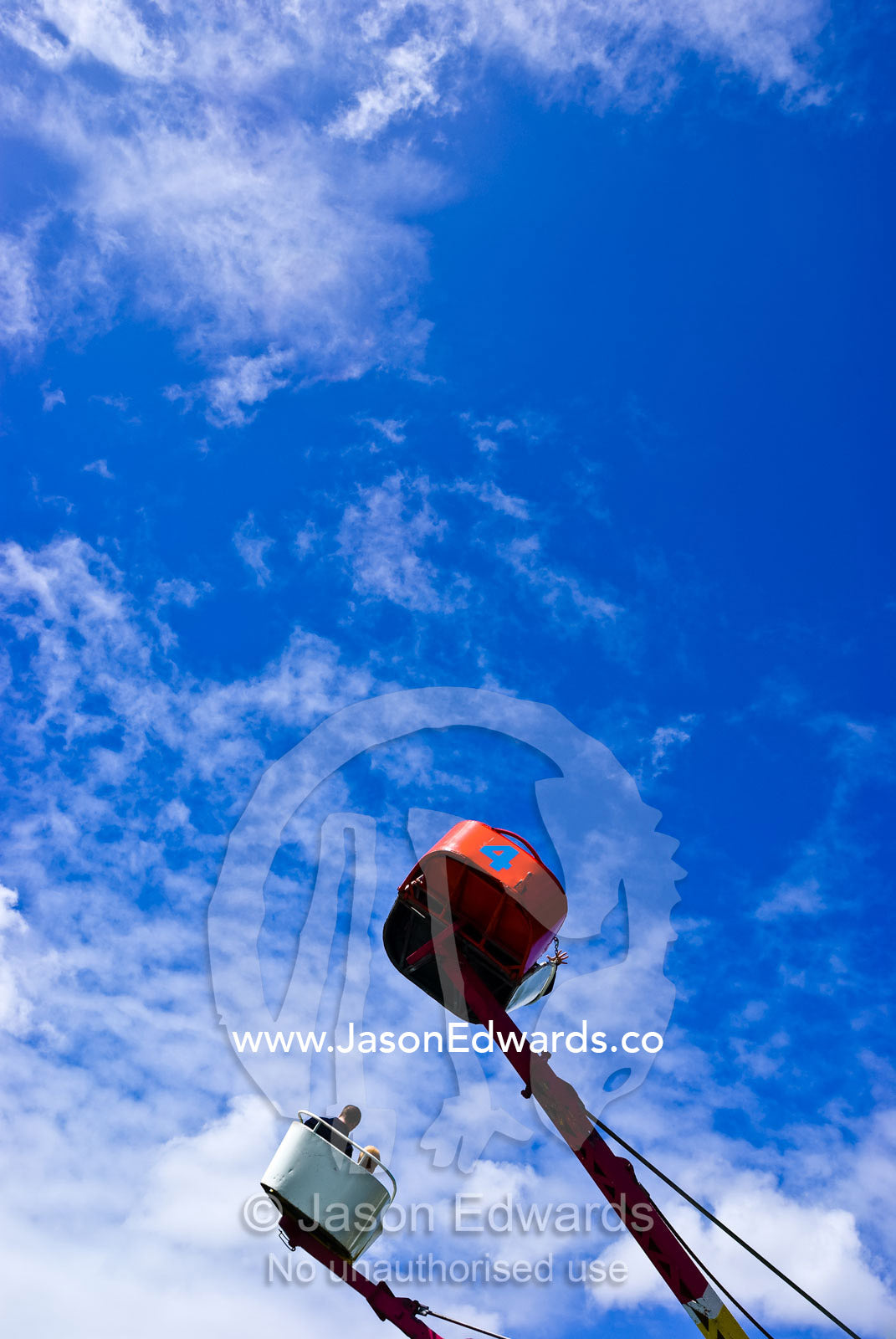 Children ride a colourful carnival ride twirling in a blue summer sky. Malvern East, Victoria, Australia