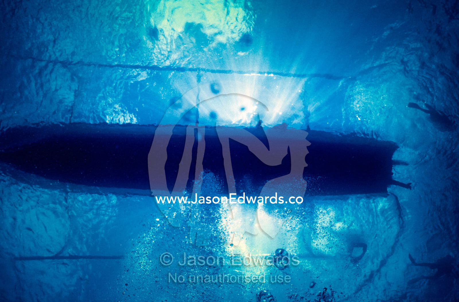 Sun rays stream past an outrigger boat collecting scuba divers. Crystal Bay, Nusa Ceningan, Nusa Penida, Bali, Indonesia.