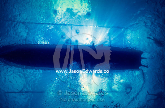 Sun rays stream past an outrigger boat collecting scuba divers. Crystal Bay, Nusa Ceningan, Nusa Penida, Bali, Indonesia.