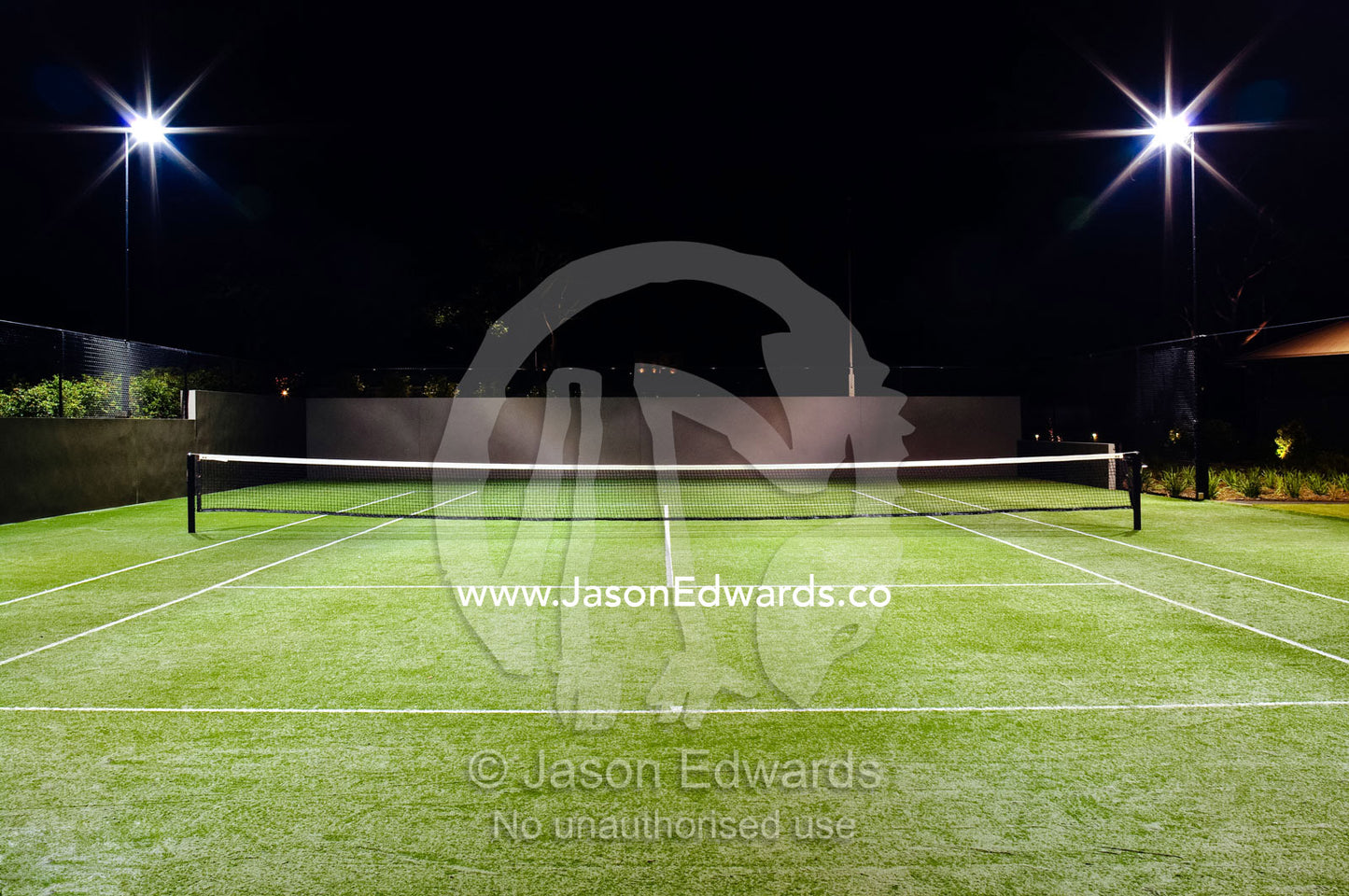 Floodlights illuminate a private tennis court on a wealthy homestead. Red Hill, Mornington Peninsula, Victoria, Australia.