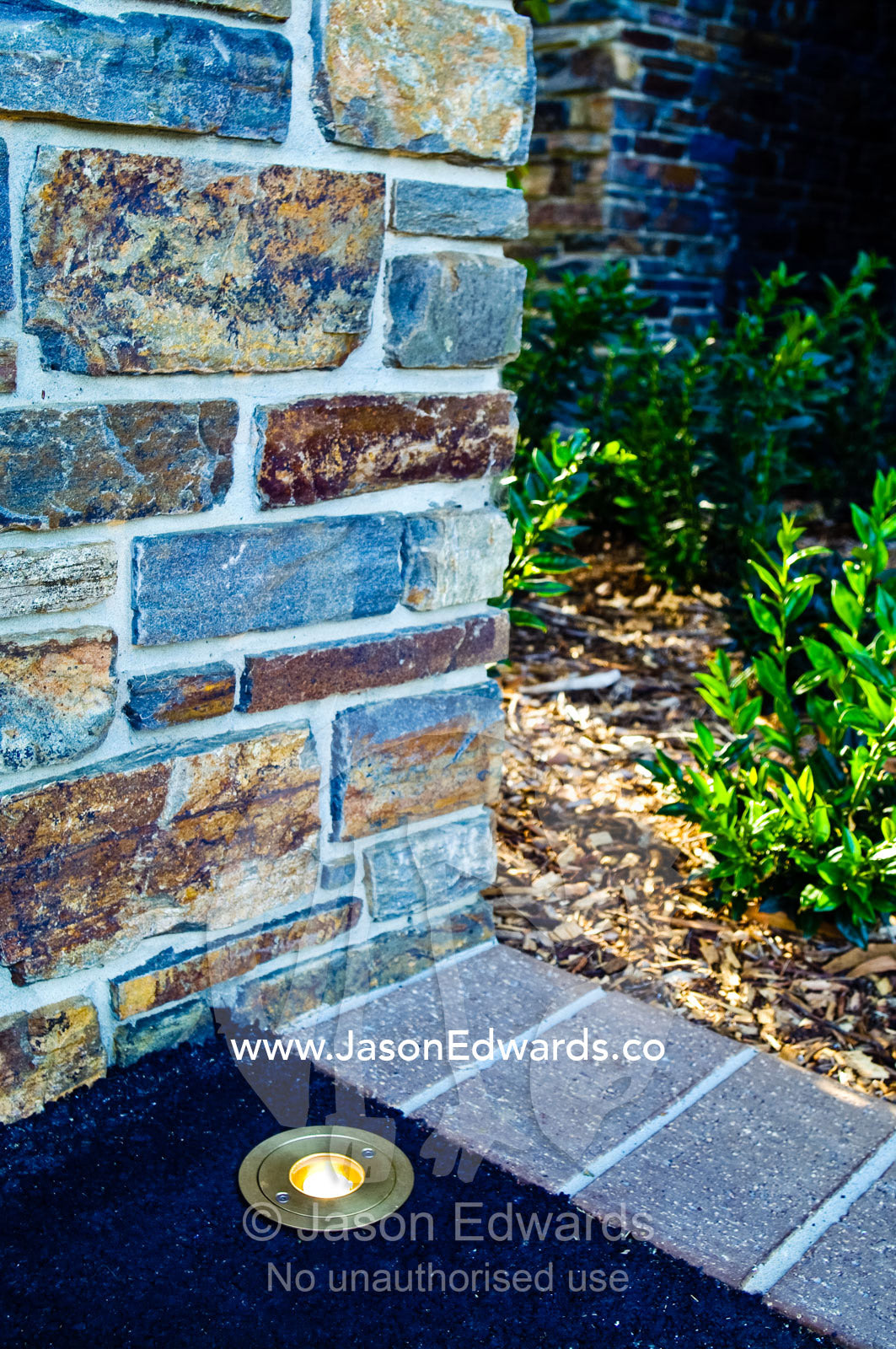 A brass lighting fixture illuminates a pathway and stone pillar. Red Hill, Mornington Peninsula, Victoria, Australia.