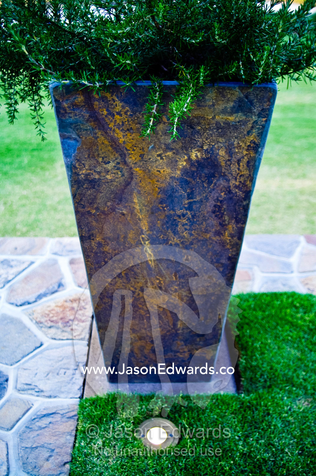 A brass lighting fixture in a garden lawn illuminates a stone potplant Red Hill, Mornington Peninsula, Victoria, Australia.