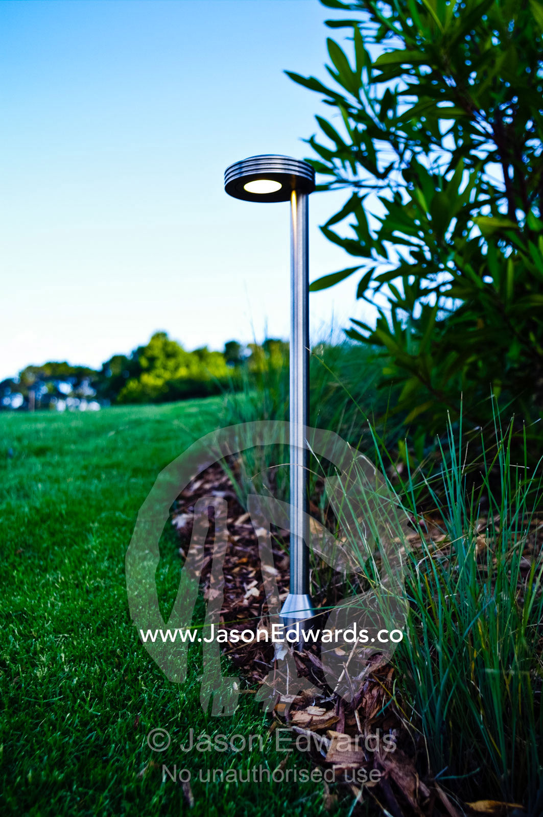 A stainless steel lighting fixture illuminates a garden bed and lawn. Red Hill, Mornington Peninsula, Victoria, Australia.