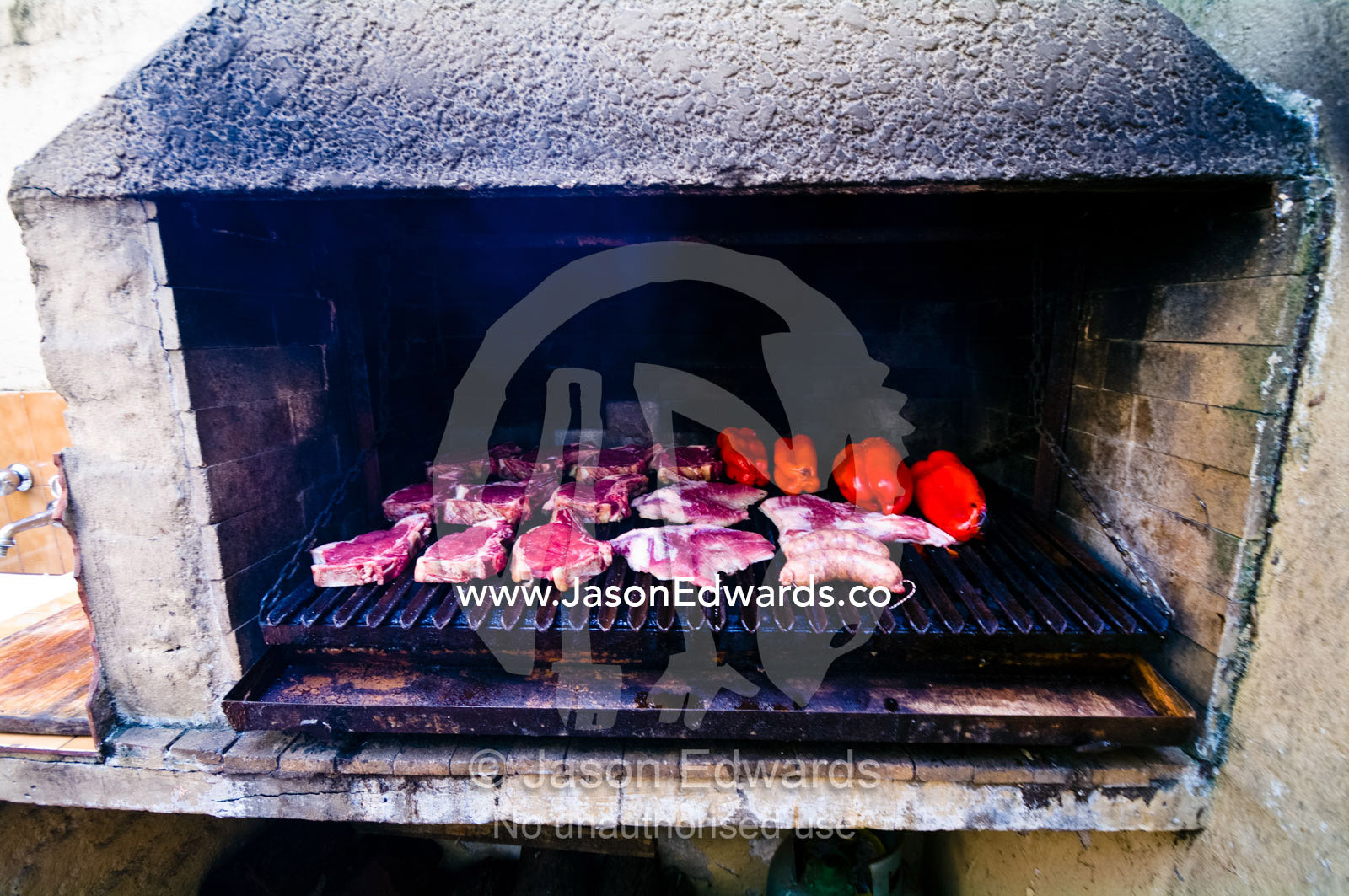 Meat cooks in a large earthen grilling barbeque known as a parrillero. Banfield, Buenos Aires, Argentina.