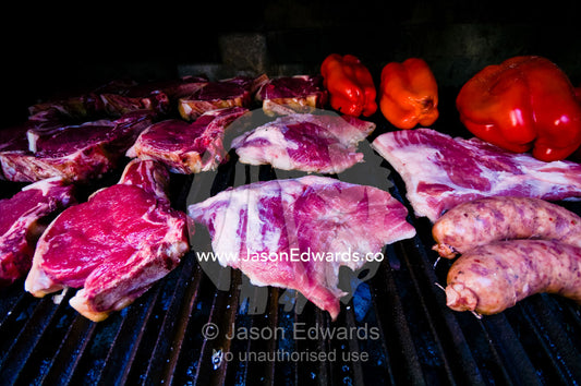 Meat cooks in a large earthen grilling barbeque known as a parrillero. Banfield, Buenos Aires, Argentina.