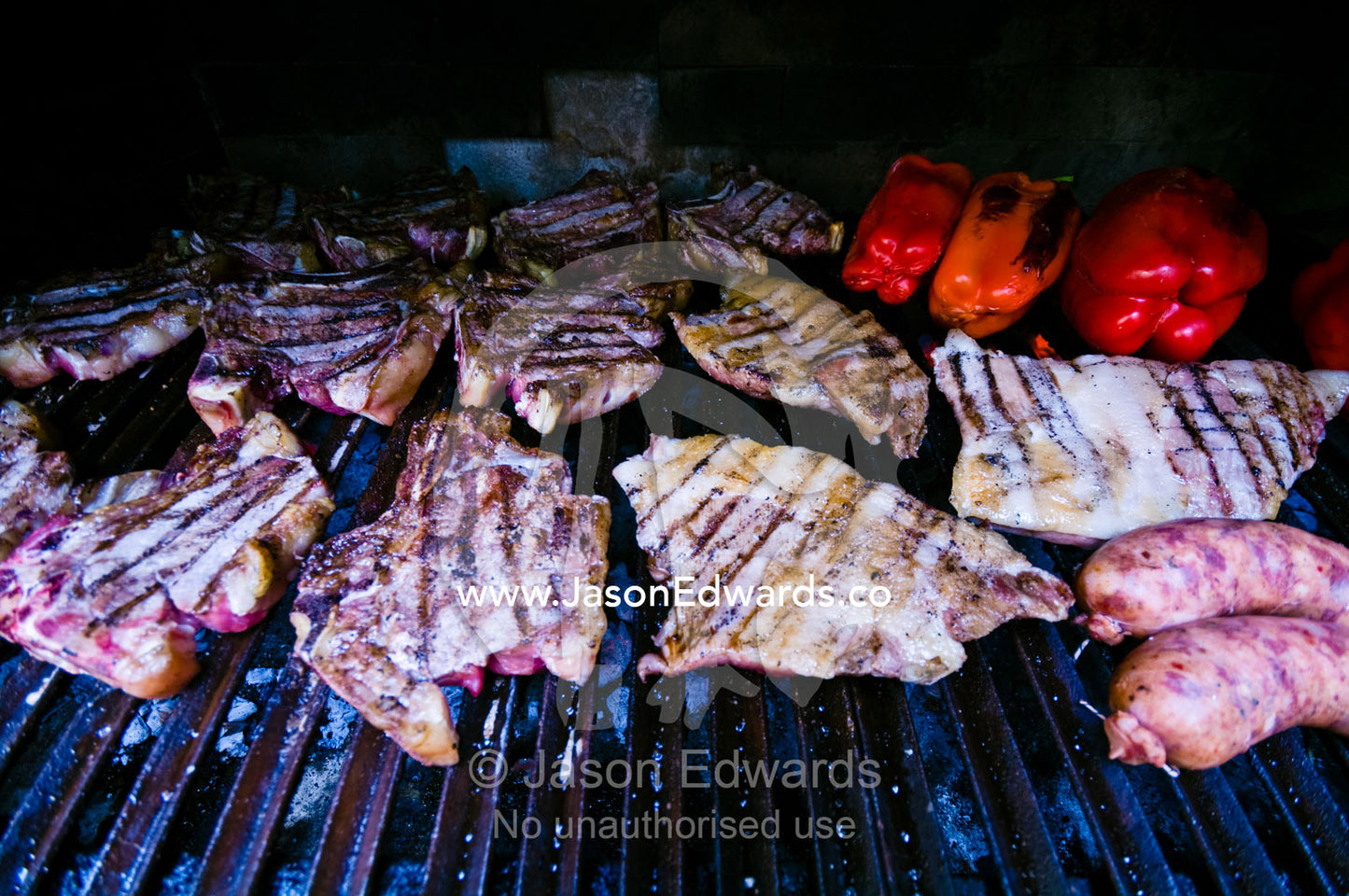Meat cooks in a large earthen grilling barbeque known as a parrillero. Banfield, Buenos Aires, Argentina.