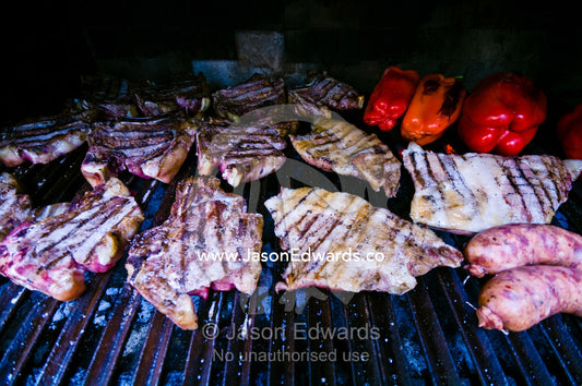 Meat cooks in a large earthen grilling barbeque known as a parrillero. Banfield, Buenos Aires, Argentina.