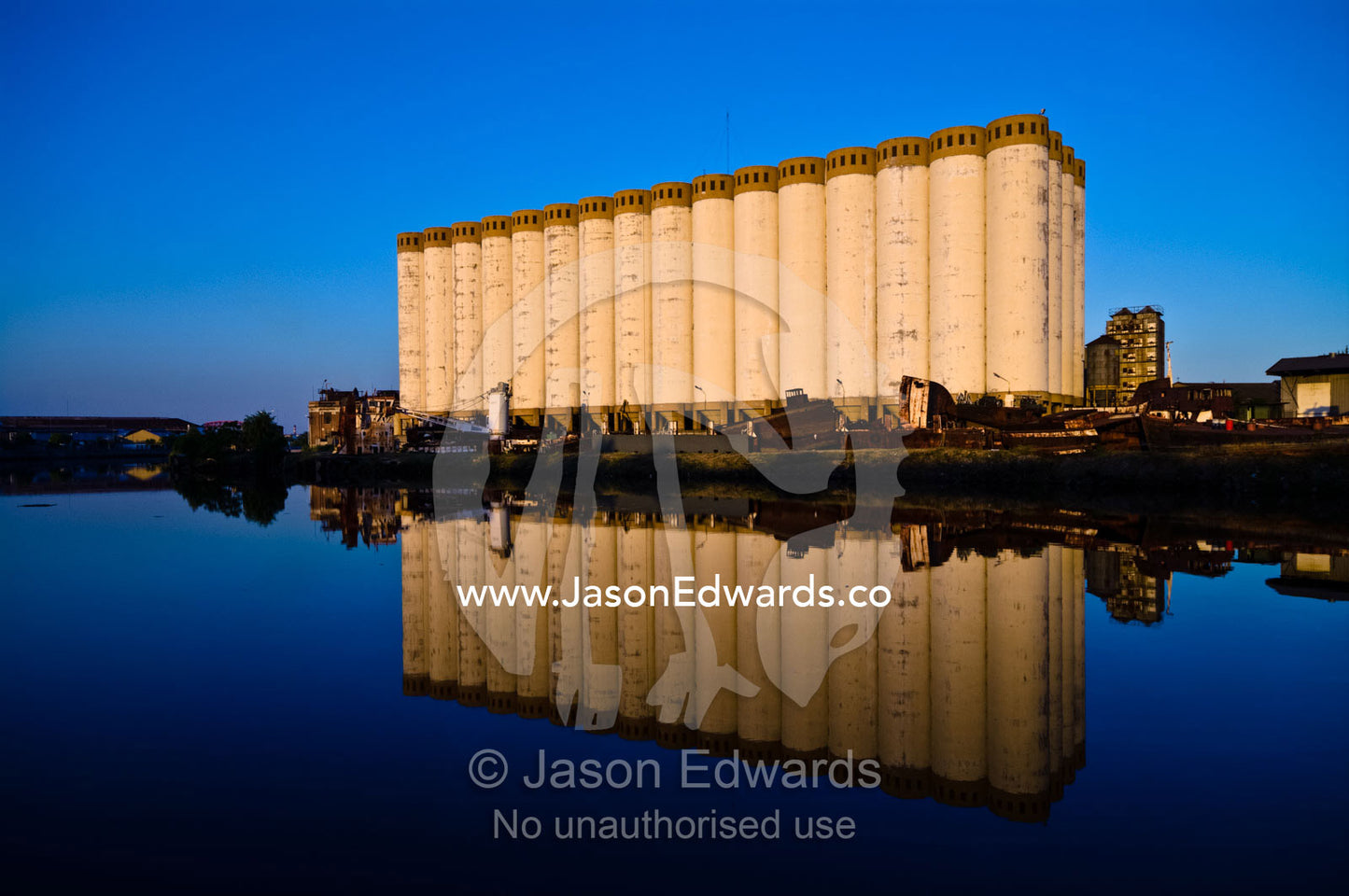 Grain silos and rusting boats reflected in the still waters of a river Riachuelo River, La Boca, Buenos Aires, Argentina.