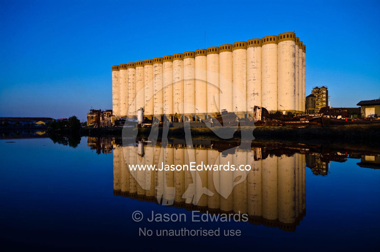 Grain silos and rusting boats reflected in the still waters of a river Riachuelo River, La Boca, Buenos Aires, Argentina.