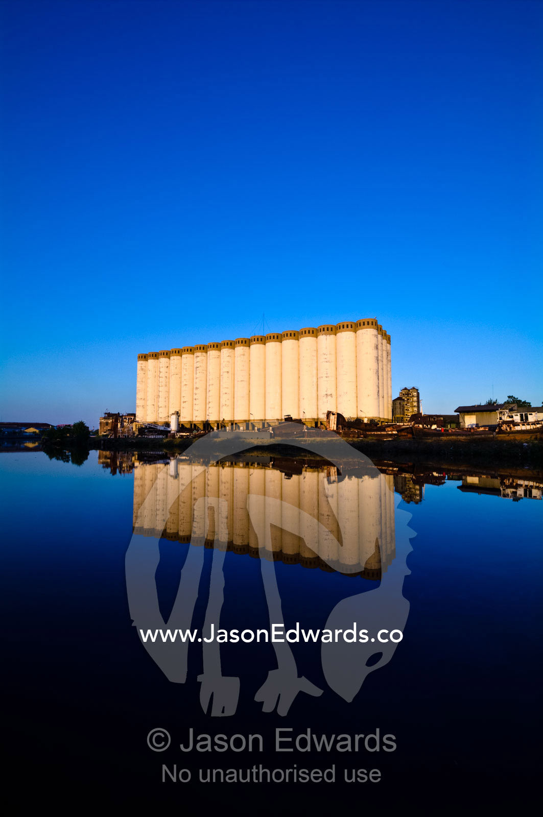 Grain silos and rusting boats reflected in the still waters of a river Riachuelo River, La Boca, Buenos Aires, Argentina.