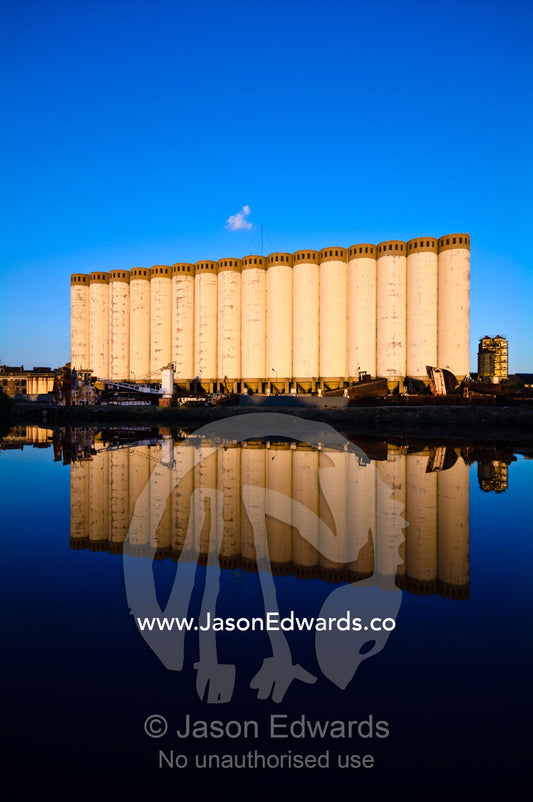 Grain silos and rusting boats reflected in the still waters of a river Riachuelo River, La Boca, Buenos Aires, Argentina.