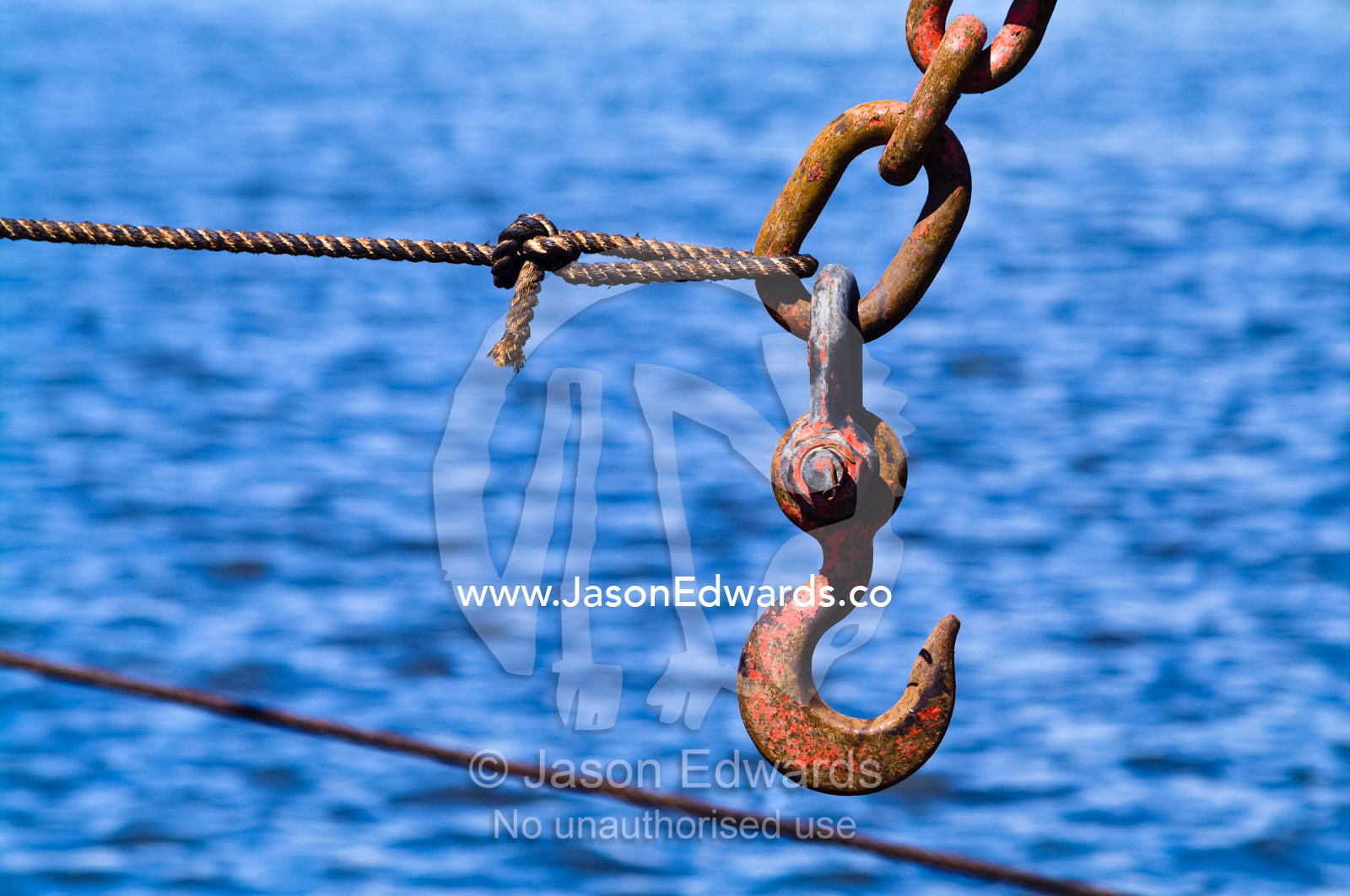 A steel cable holds a chain and hook from a crane above a river port. La Riachuelo, Little River, La Boca, Buenos Aires, Argentina.