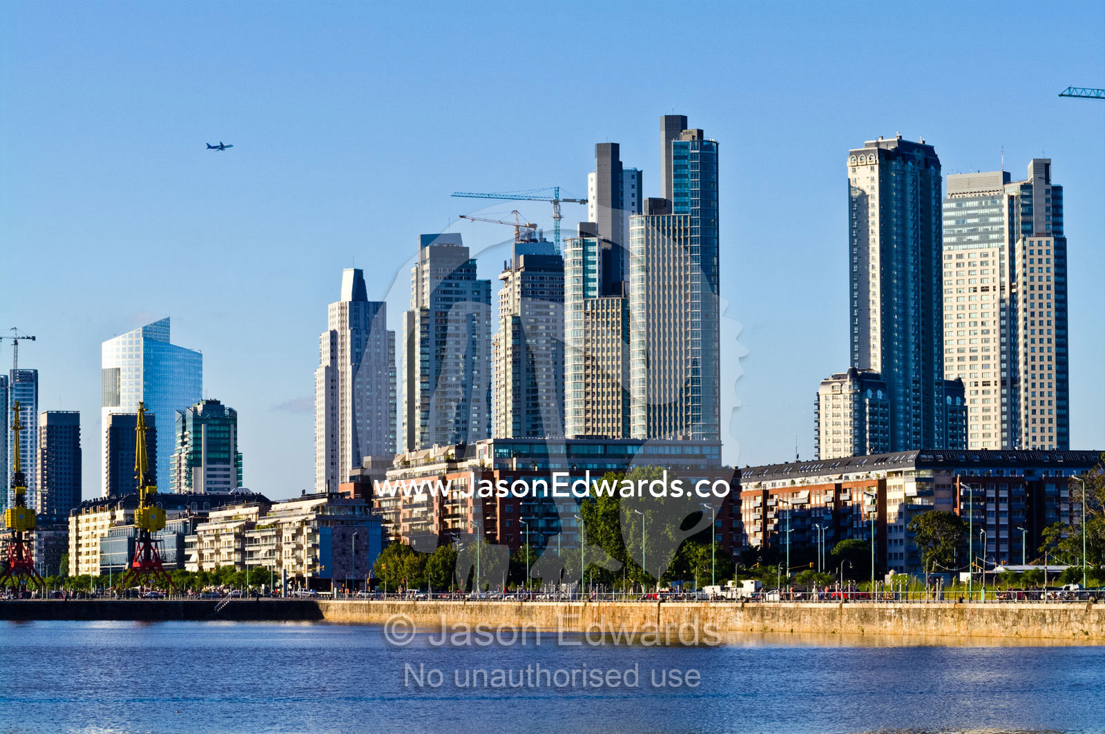 A passenger airline flies over a new city skyline under construction. Puerto Madero, Buenos Aires, Argentina.