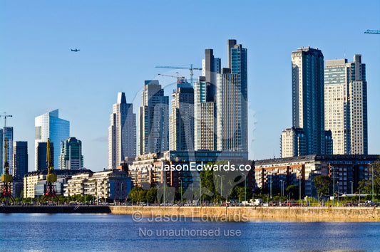 A passenger airline flies over a new city skyline under construction. Puerto Madero, Buenos Aires, Argentina.