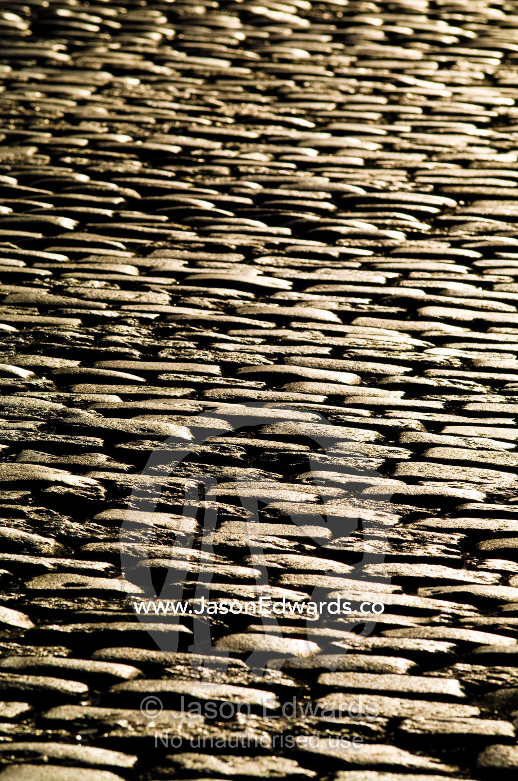 Golden sunlight falls on the textured surface of a cobblestone road. Calle Defensa, San Telmo, Buenos Aires, Argentina.