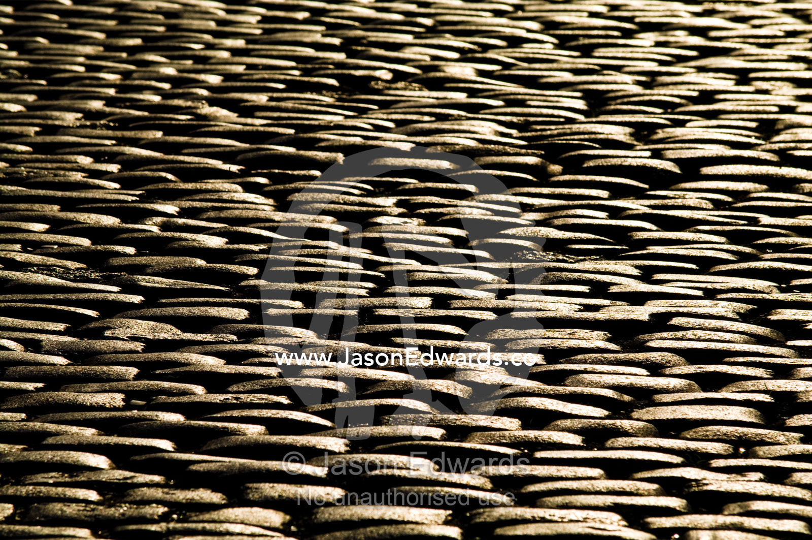 Golden sunlight falls on the textured surface of a cobblestone road. Calle Defensa, San Telmo, Buenos Aires, Argentina.