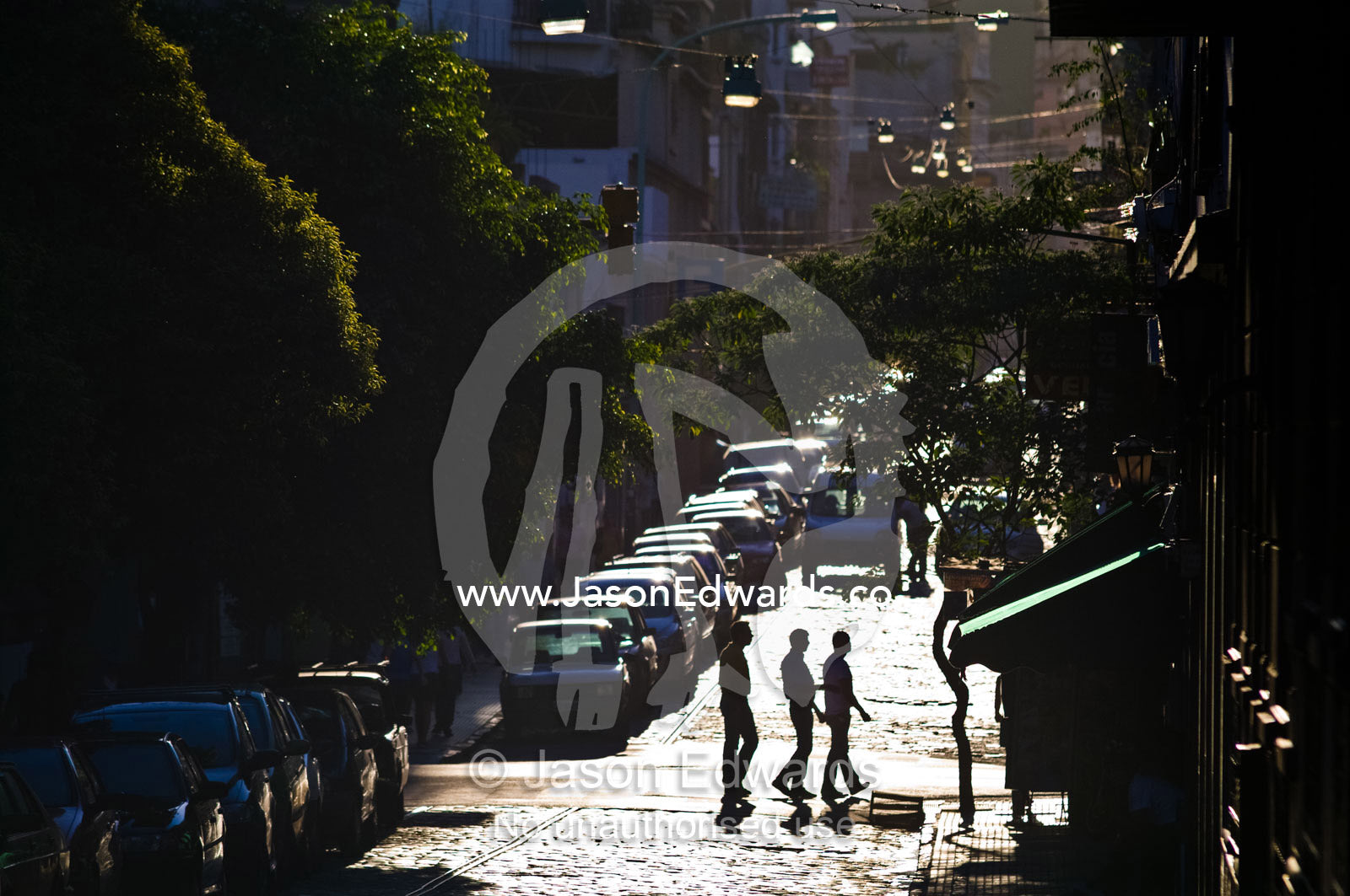 Friends crossing an inner city street backlit by the setting sun. San Telmo, Buenos Aires, Argentina.