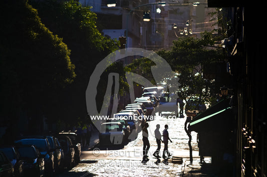 Friends crossing an inner city street backlit by the setting sun. San Telmo, Buenos Aires, Argentina.