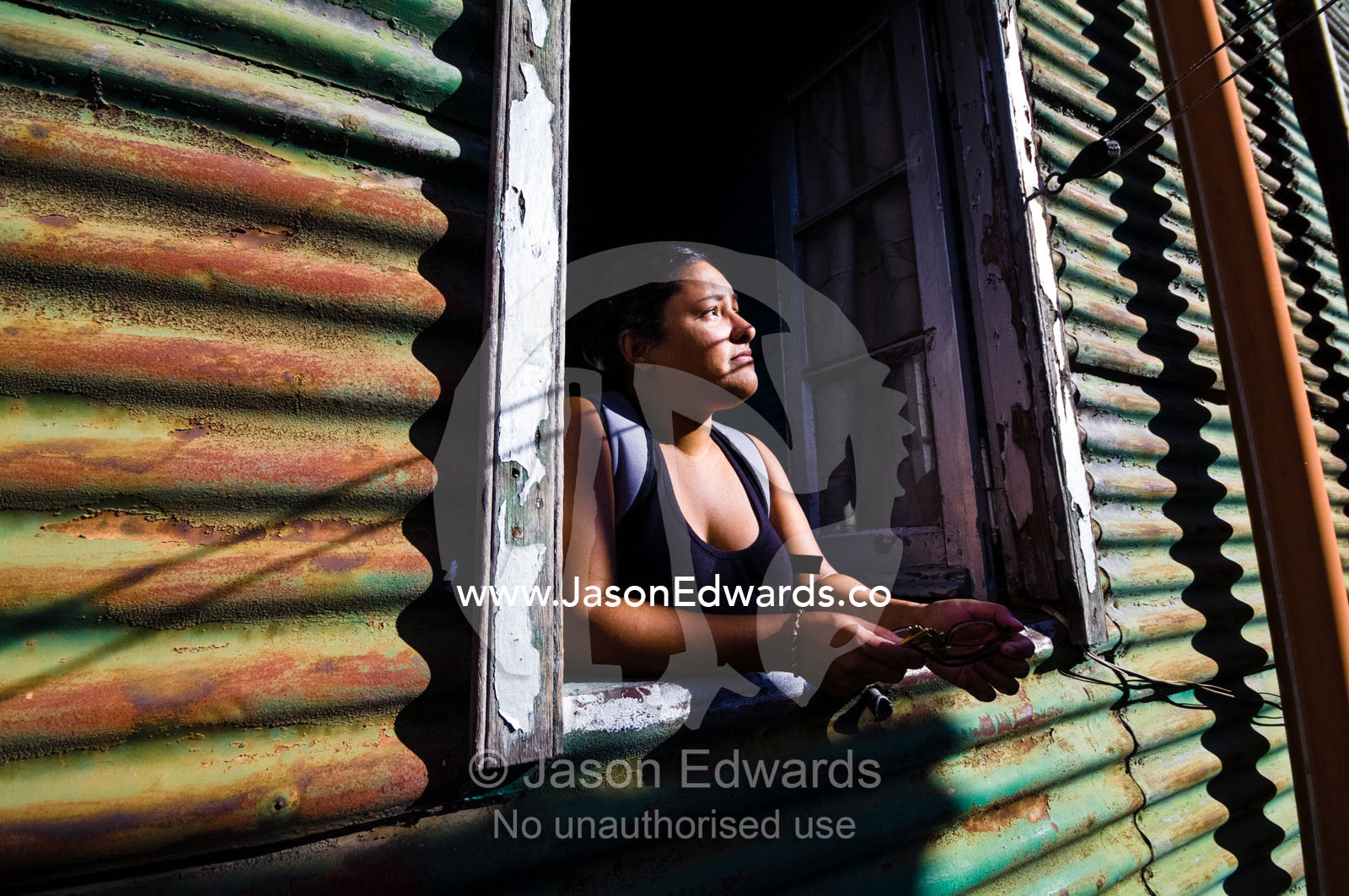 A young woman looks from the window of a corrugated tin conventillo. La Boca, Buenos Aires, Argentina.