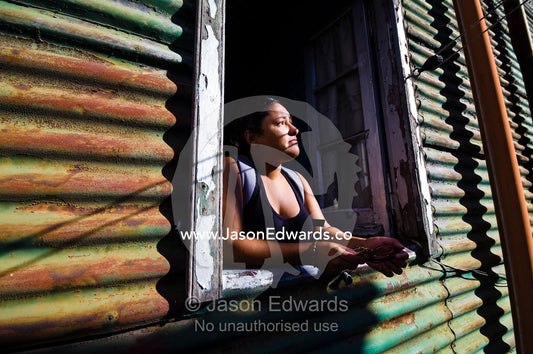 A young woman looks from the window of a corrugated tin conventillo. La Boca, Buenos Aires, Argentina.