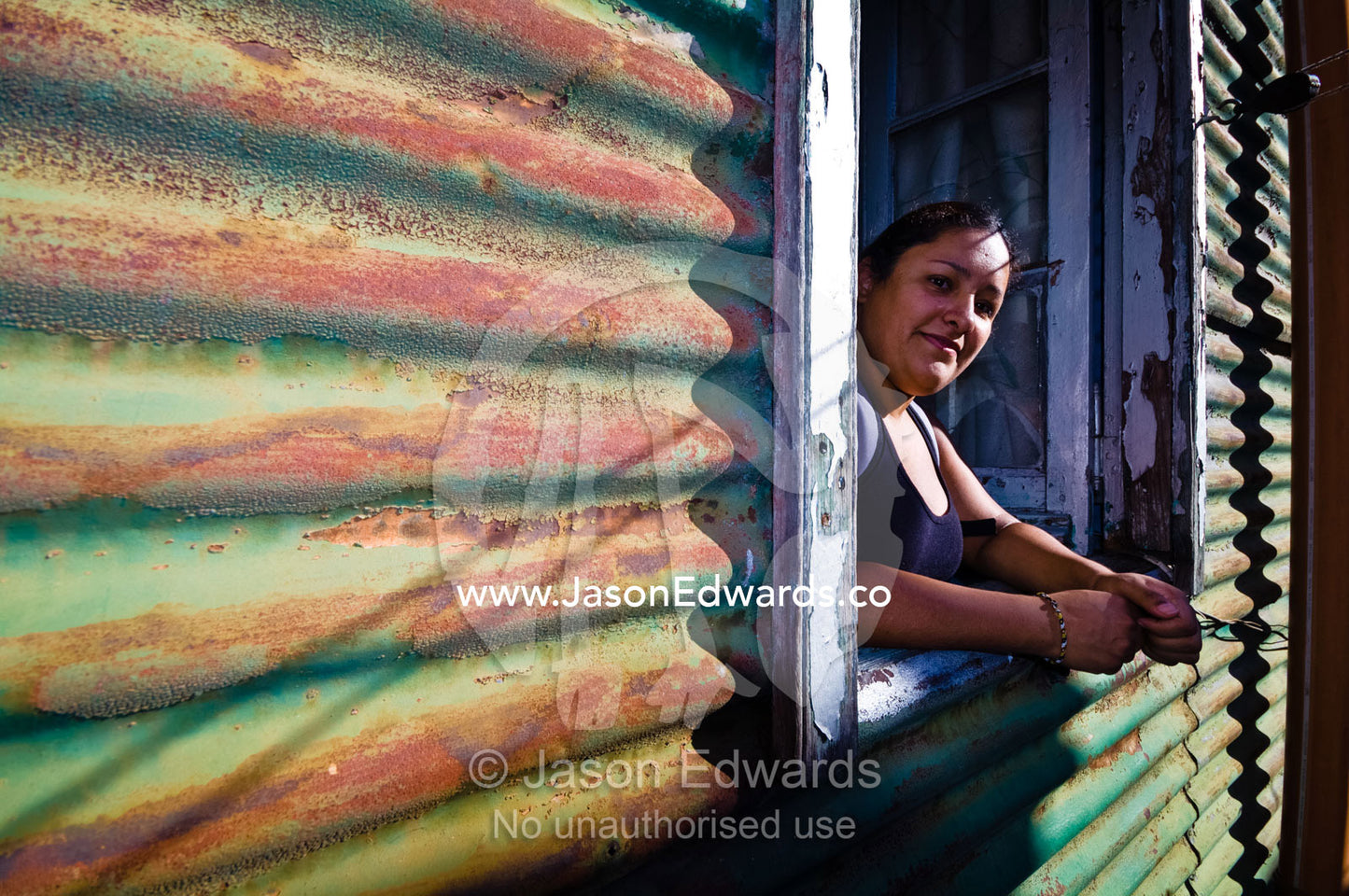 A young woman looks from the window of a corrugated tin conventillo. La Boca, Buenos Aires, Argentina.