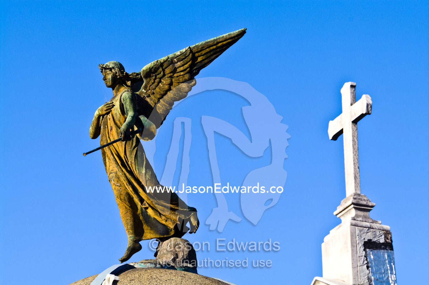 A brass statue of an angel and crucifix on the roof of a mausoleum. La Recoleta Cemetery, Recoleta, Buenos Aires, Argentina.