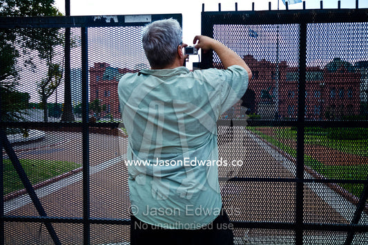 A tourist photographs the Casa Rosada through a steel security fence. Plaza de Mayo, Buenos Aires, Argentina.