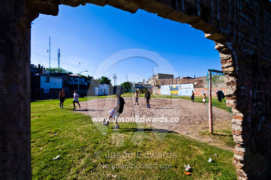 Boys play football on vacant land surrounded by crumbling brick walls. La Boca, Buenos Aires, Argentina.