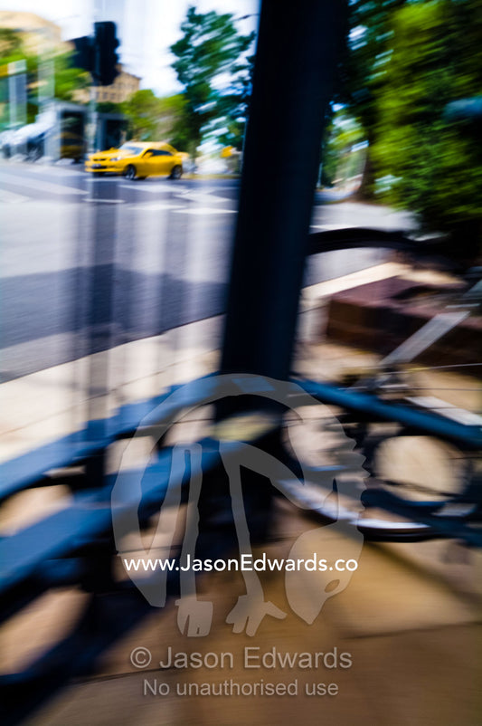 A bright yellow car speeding down a street viewed through a fence. North Melbourne, Melbourne, Victoria, Australia.