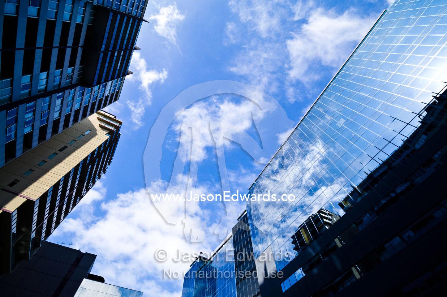 Blue sky and fluffy clouds reflect in the windows of an office block. St Kilda Road, Melbourne, Victoria, Australia.